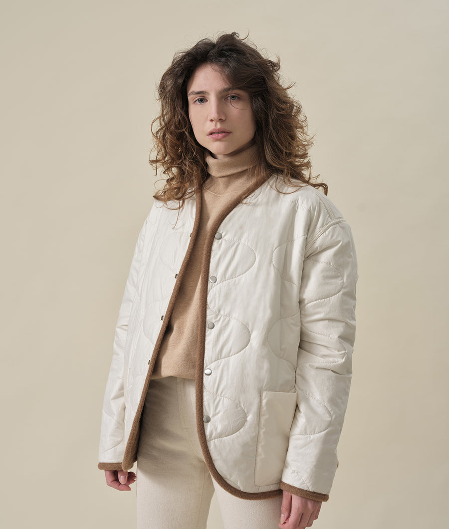The person is wearing a white quilted jacket with a beige turtleneck sweater. - Industry of All Nations