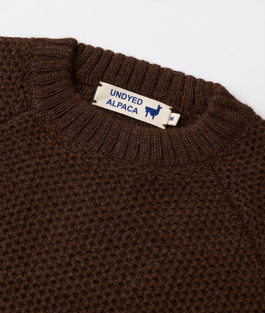 A close-up detail shot of a brown knitted alpaca sweater with a label that says "UNDYED ALPACA" - Industry of All Nations