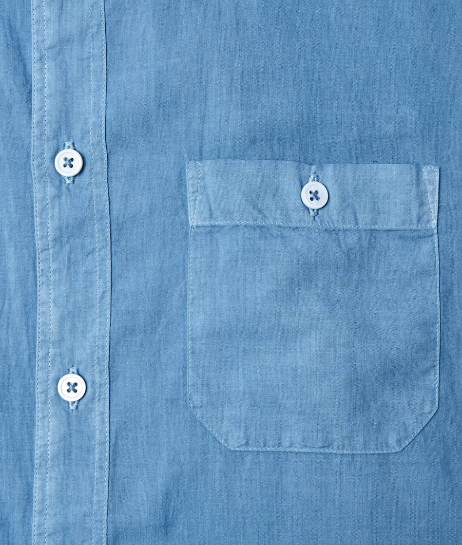 Flat lay detail of a blue chambray shirt with white buttons and a chest pocket - Industry of All Nations