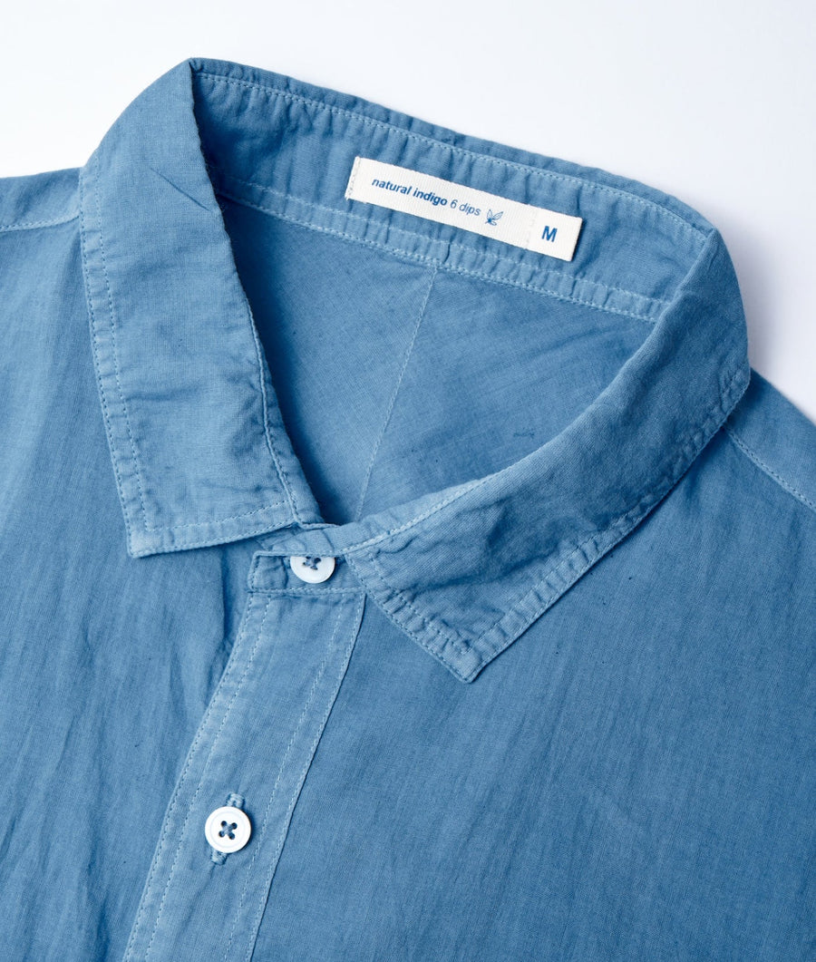 A blue cotton shirt with a collar, button-down front, and a 'natural indigo 6 dips' label displayed flat on a white background - Industry of All Nations