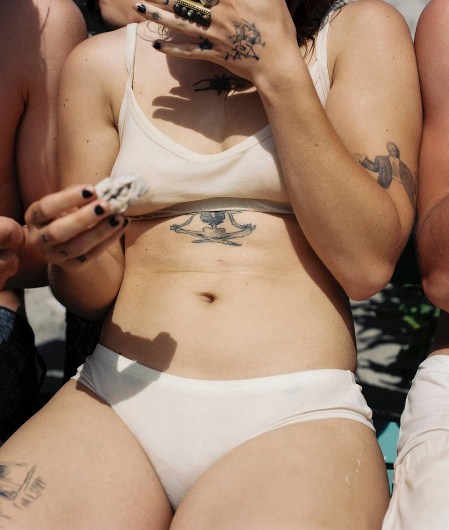 A white tank top and underwear worn by a person with tattoos on the arms - Industry of All Nations.