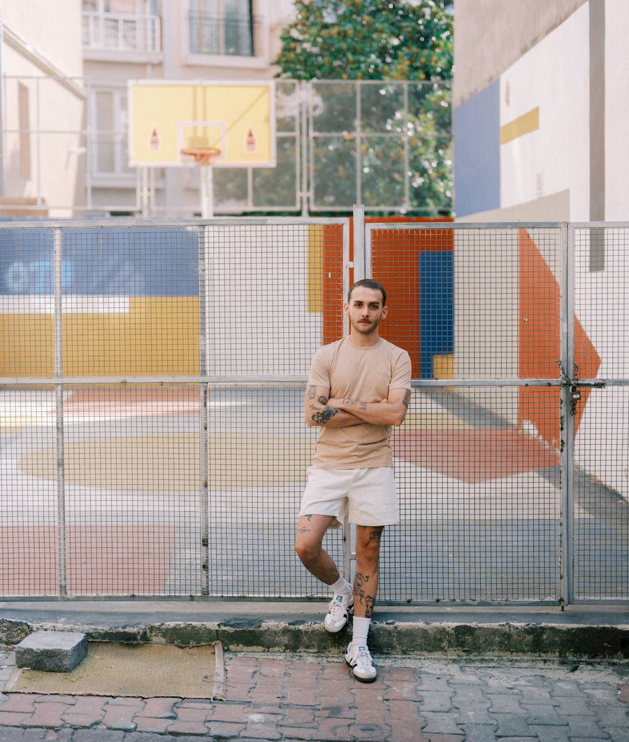 A man wearing a beige t-shirt and shorts standing in front of a colorful basketball court - Industry of All Nations