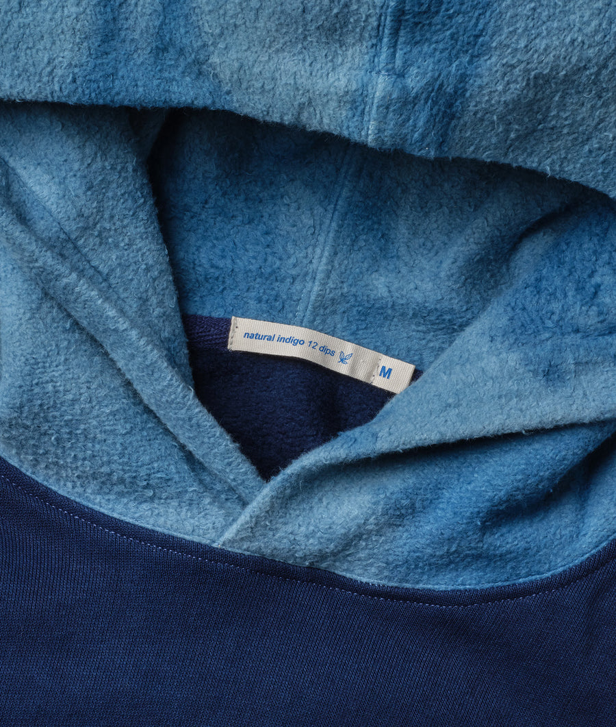 A close-up detail shot of a blue, fluffy natural indigo hooded sweatshirt with a size tag - Industry of All Nations