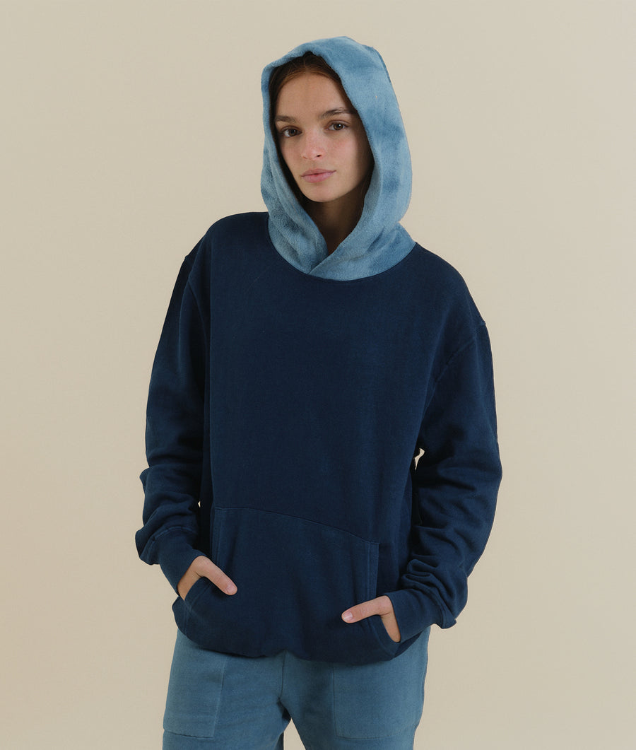 A young woman wearing a navy blue hooded sweatshirt with a light blue hood - Industry of All Nations