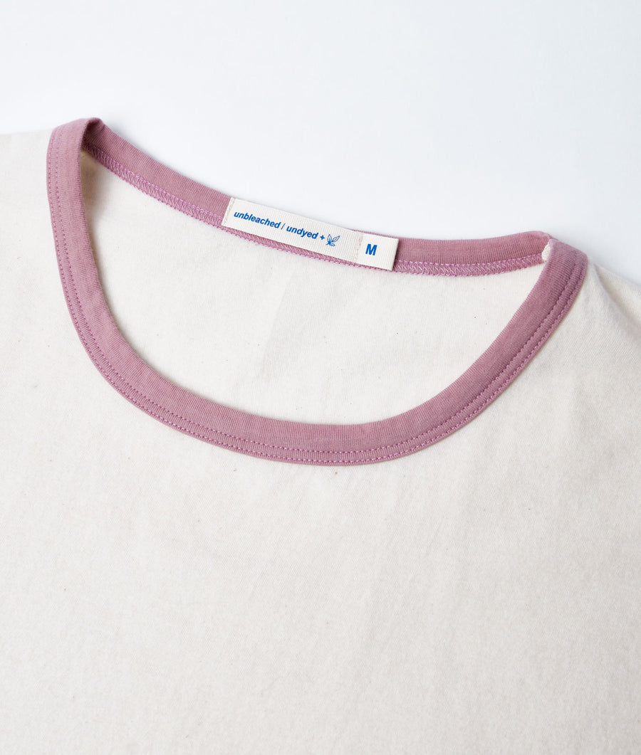 Flat lay image of a medium-size white cotton t-shirt with a pink neckline and an "unbleached/undyed" label - Industry of All Nations