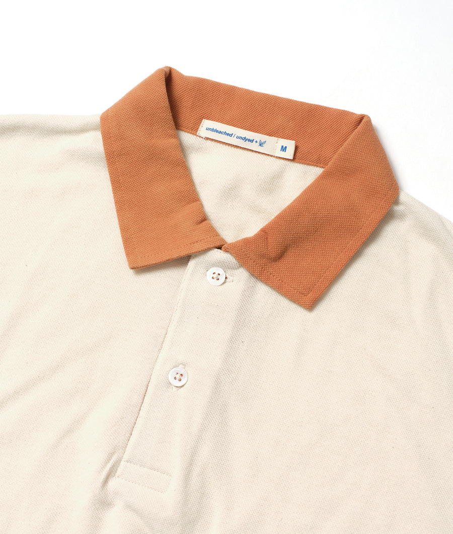 Flatlay of an unbleached and undyed organic cotton polo shirt in a warm orange color - Industry of All Nations