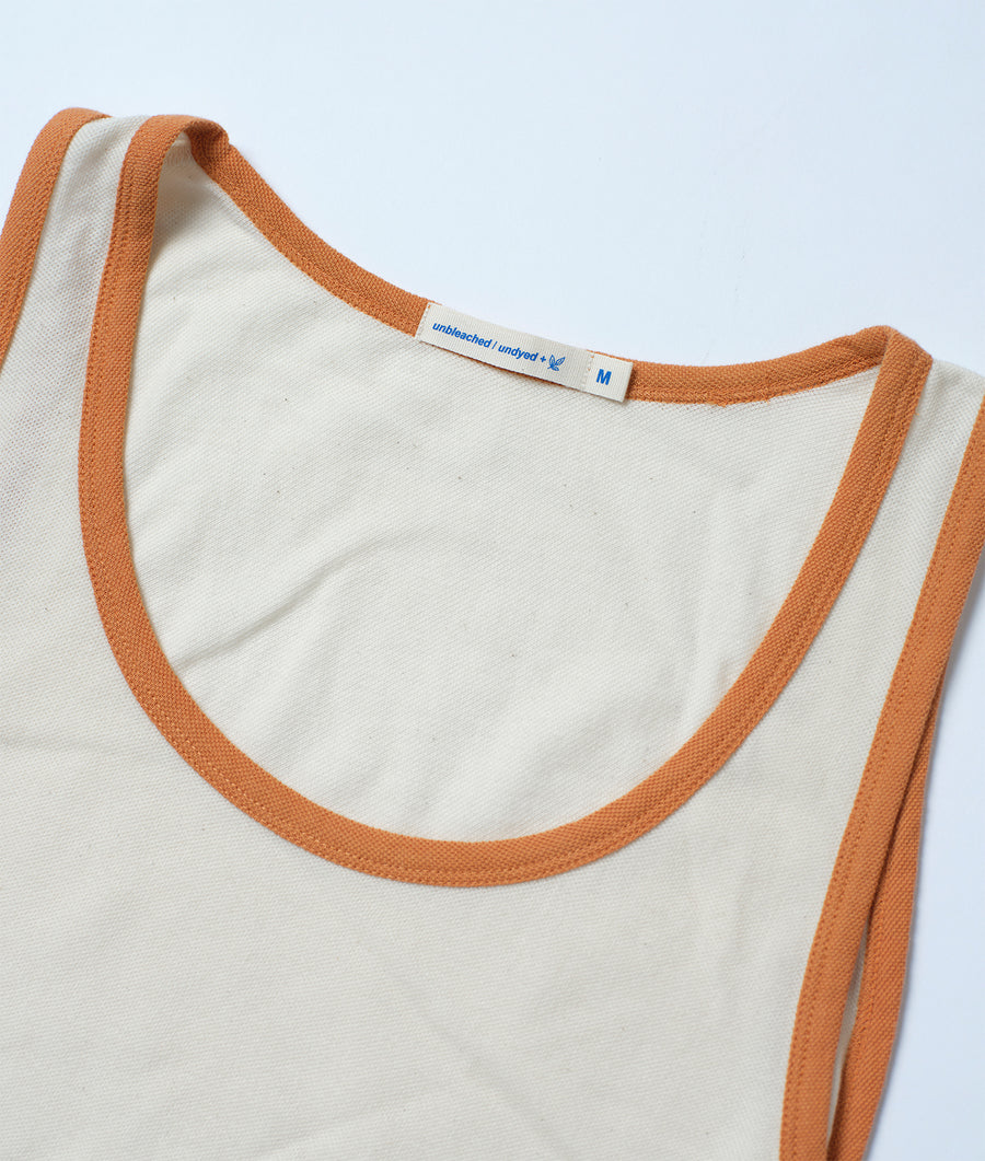 Flat lay shot of a white sleeveless top with orange trim and an unbleached label - Industry of All Nations