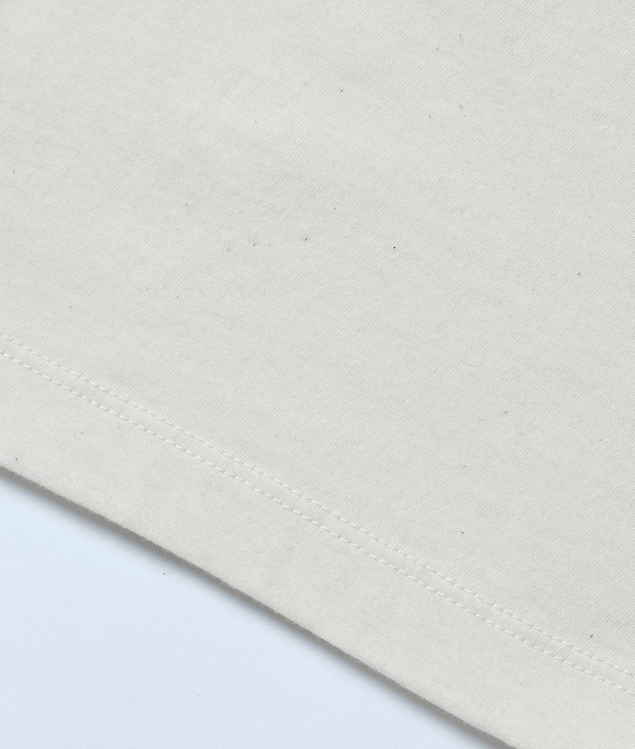 Flat lay shot of a light-colored fabric with visible stitching, likely an organic cotton garment from Industry of All Nations.