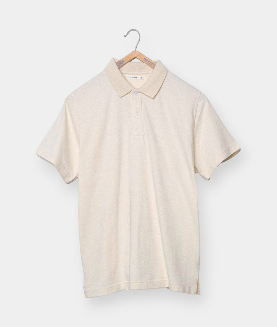 A beige, short-sleeved polo shirt displayed on a wooden hanger - Industry of All Nations