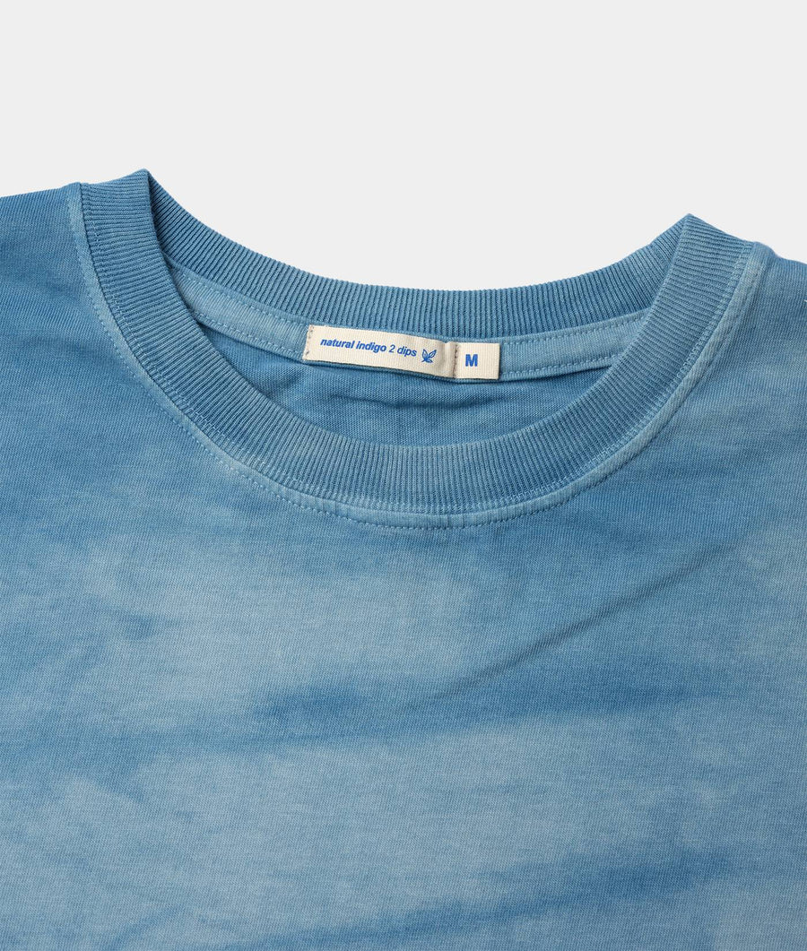 Detail shot of a light blue short-sleeve t-shirt with ribbing around the neckline, displaying the "natural indigo 2 dips" label - Industry of All Nations.