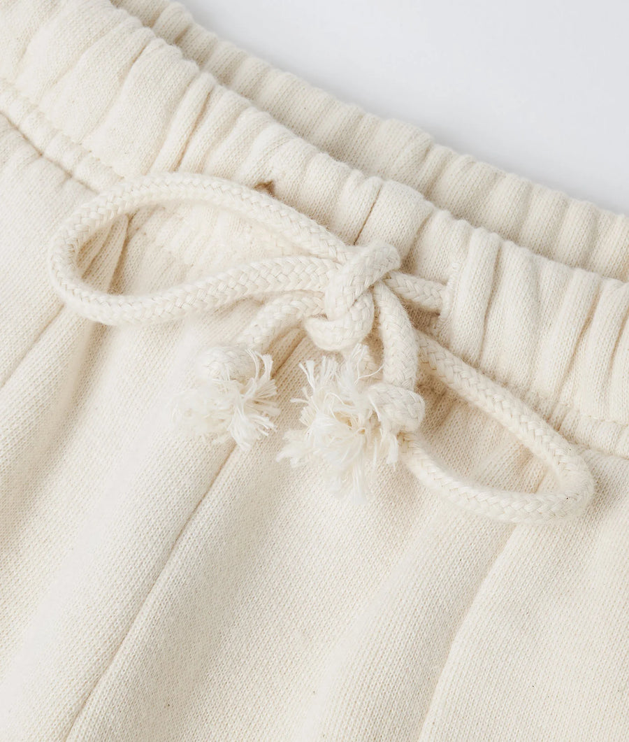 Detail shot of a cream-colored organic cotton sweatpant with a drawstring waist and frayed edges - Industry of All Nations