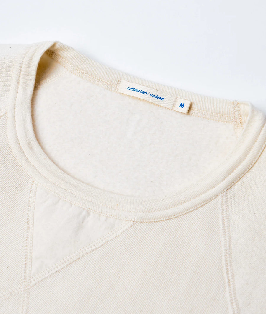 Close-up detail shot of a cream-colored organic cotton undershirt with "unbleached/undyed" label - Industry of All Nations