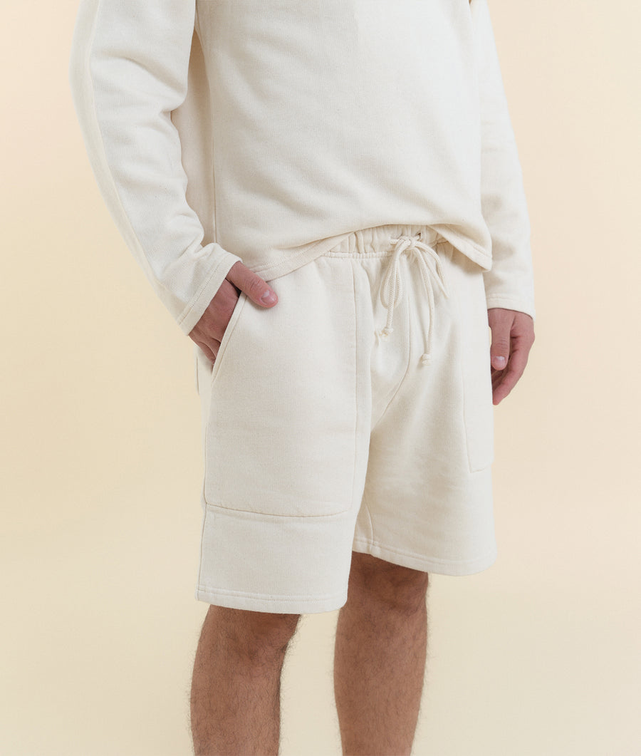 Cream-colored organic cotton sweatshorts with a drawstring waist, worn by a model - Industry of All Nations
