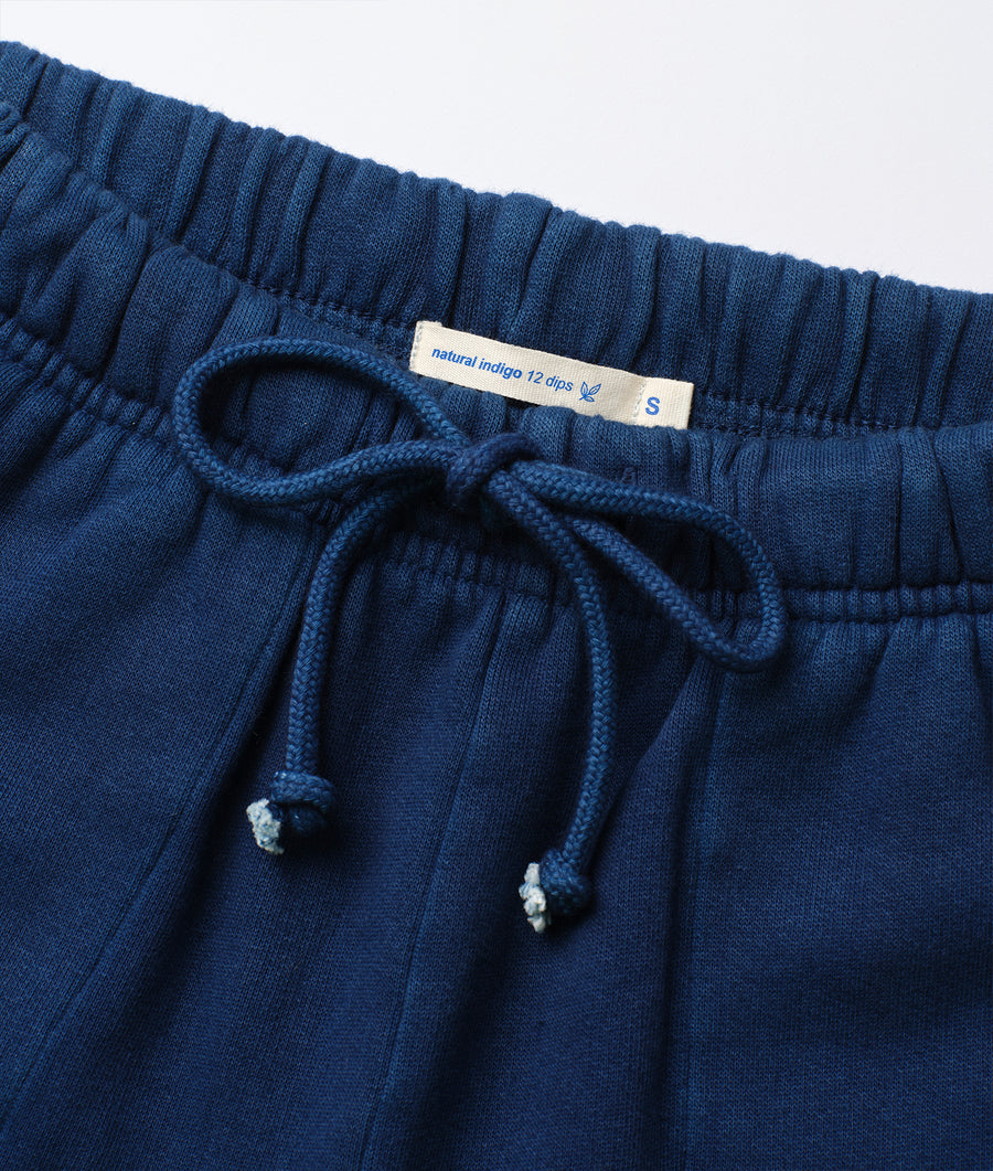 A close-up detail shot of a pair of navy blue cotton drawstring pants with the "natural indigo 12 dips" label - Industry of All Nations