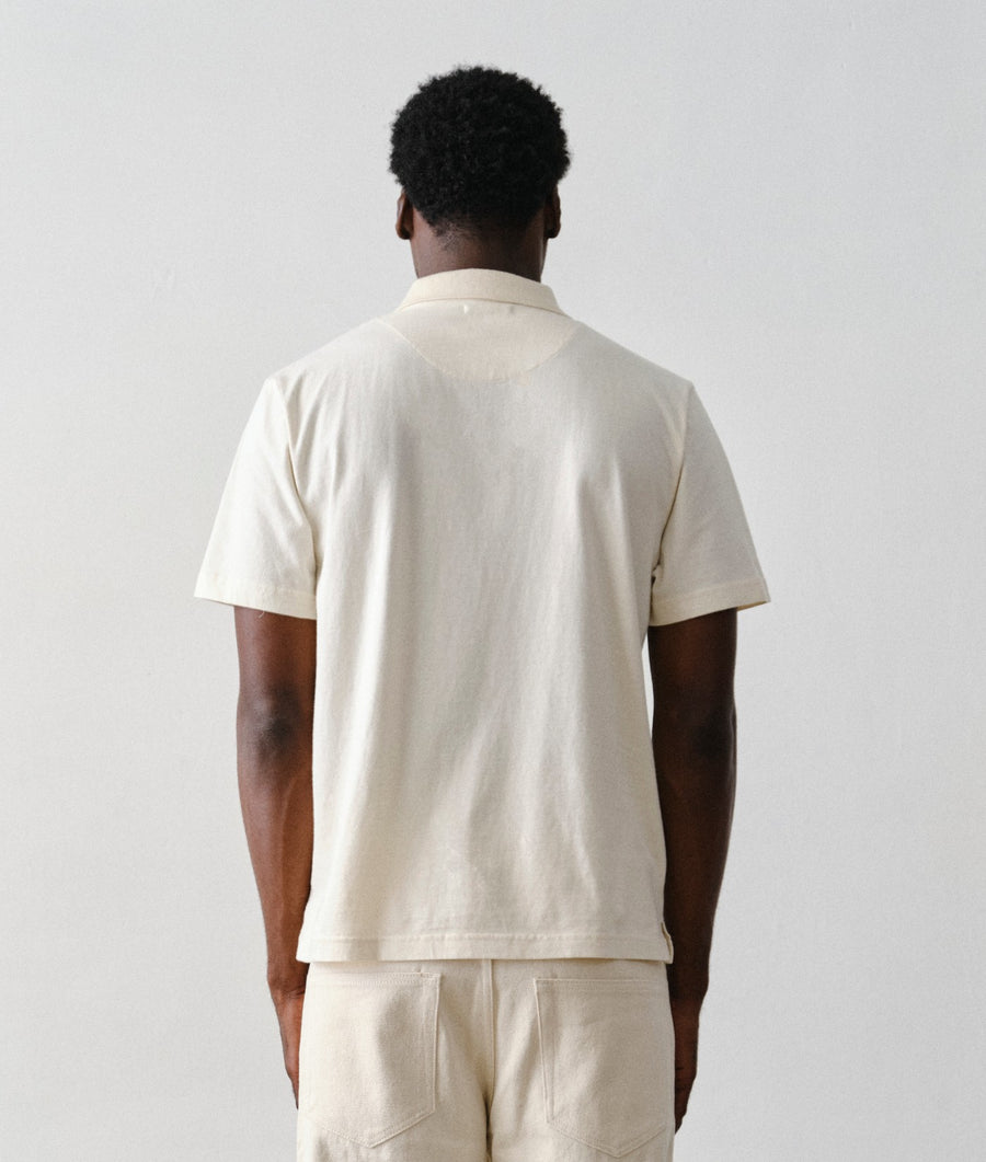 Man wearing the IOAN Standard Polo in Undyed with matching trousers, shown from the back against a plain light gray studio background.