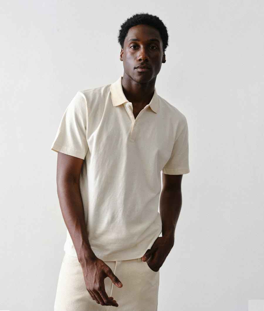 Man wearing the IOAN Standard Polo in Undyed with matching trousers, standing against a plain light gray studio background.