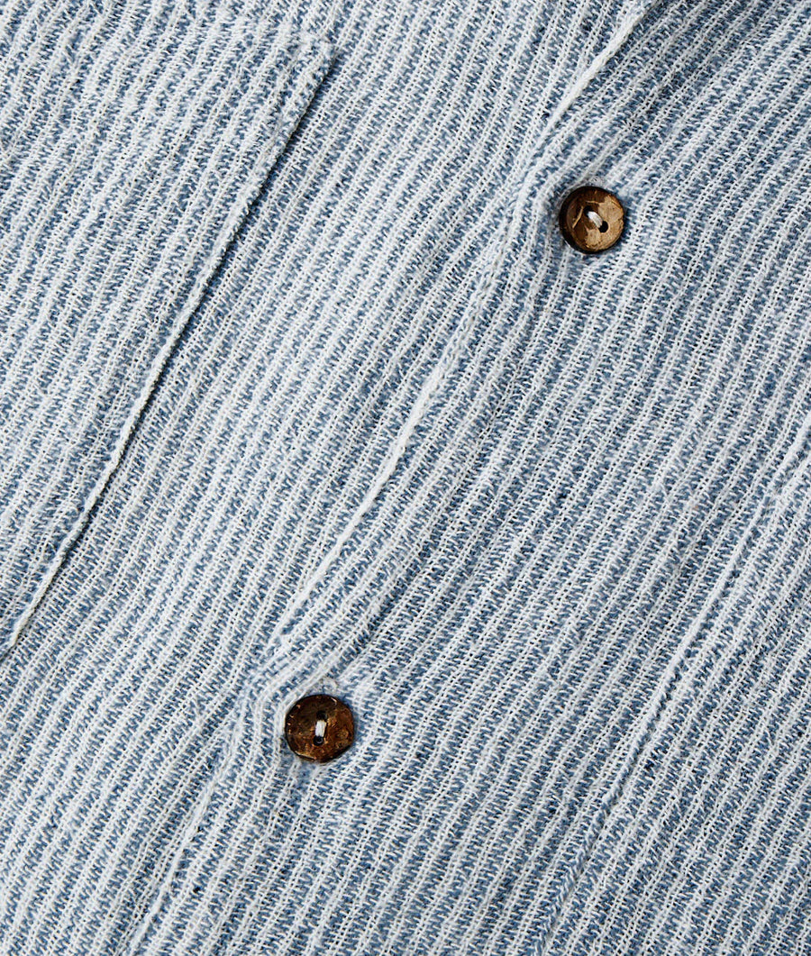 Close-up detail shot of a light blue denim jacket with brown buttons - Industry of All Nations