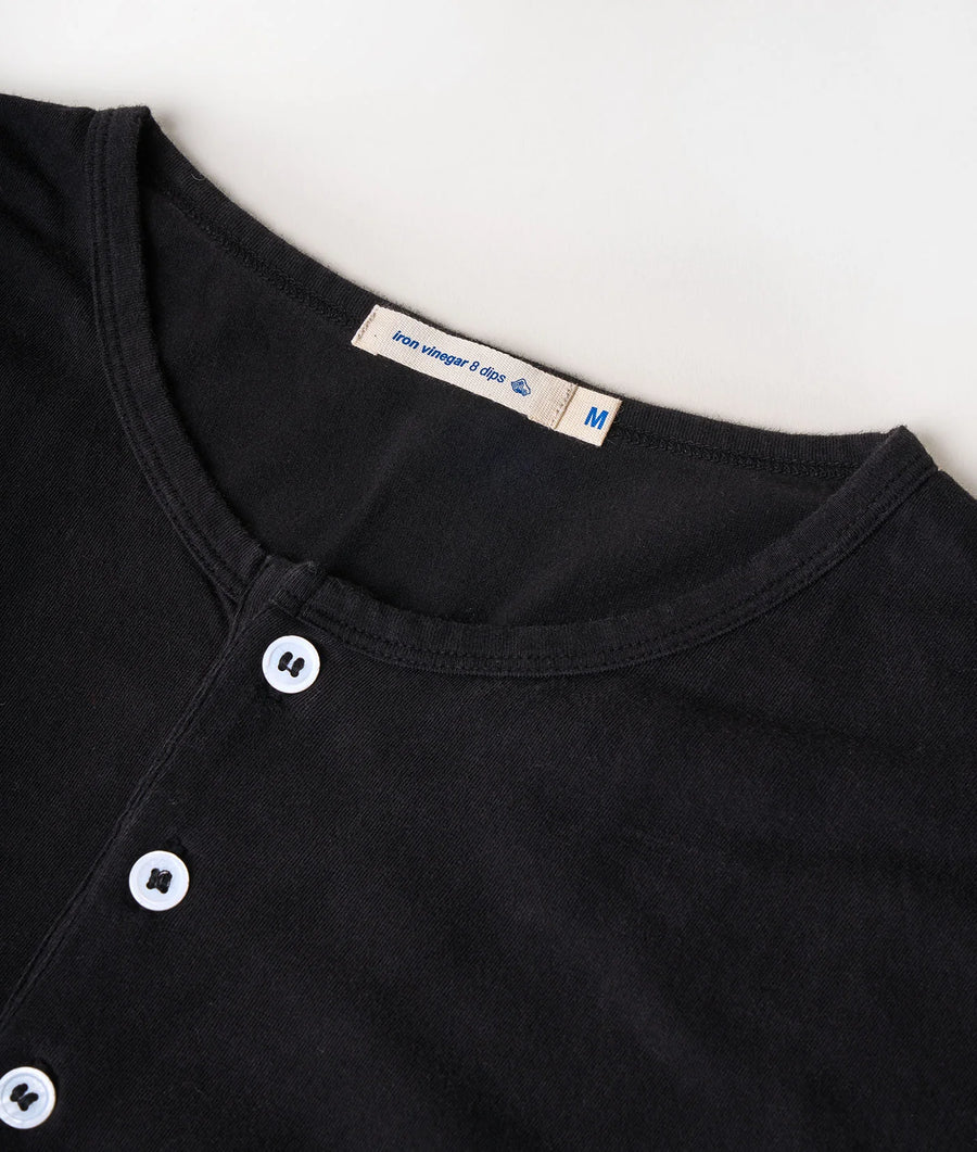 Close-up detail shot of a black organic cotton t-shirt with buttons and an "Iron vinegar 8 dips" label - Industry of All Nations