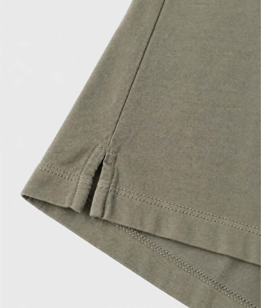 Close-up of a folded garment corner showing a muted olive green fabric with neat stitching on a light gray background.