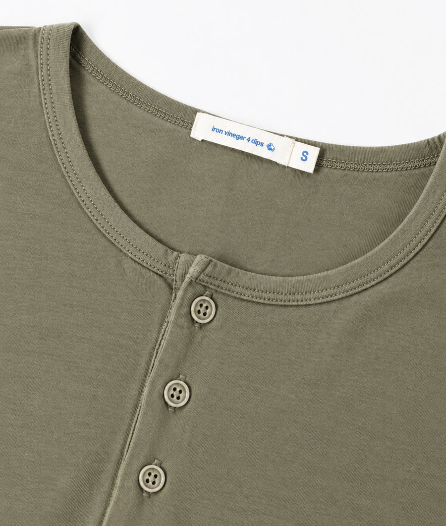 Close-up of an olive green henley shirt showing the inner neck label with 'pure color 4-color' and a size 'S' marking, plus three buttons on the chest.