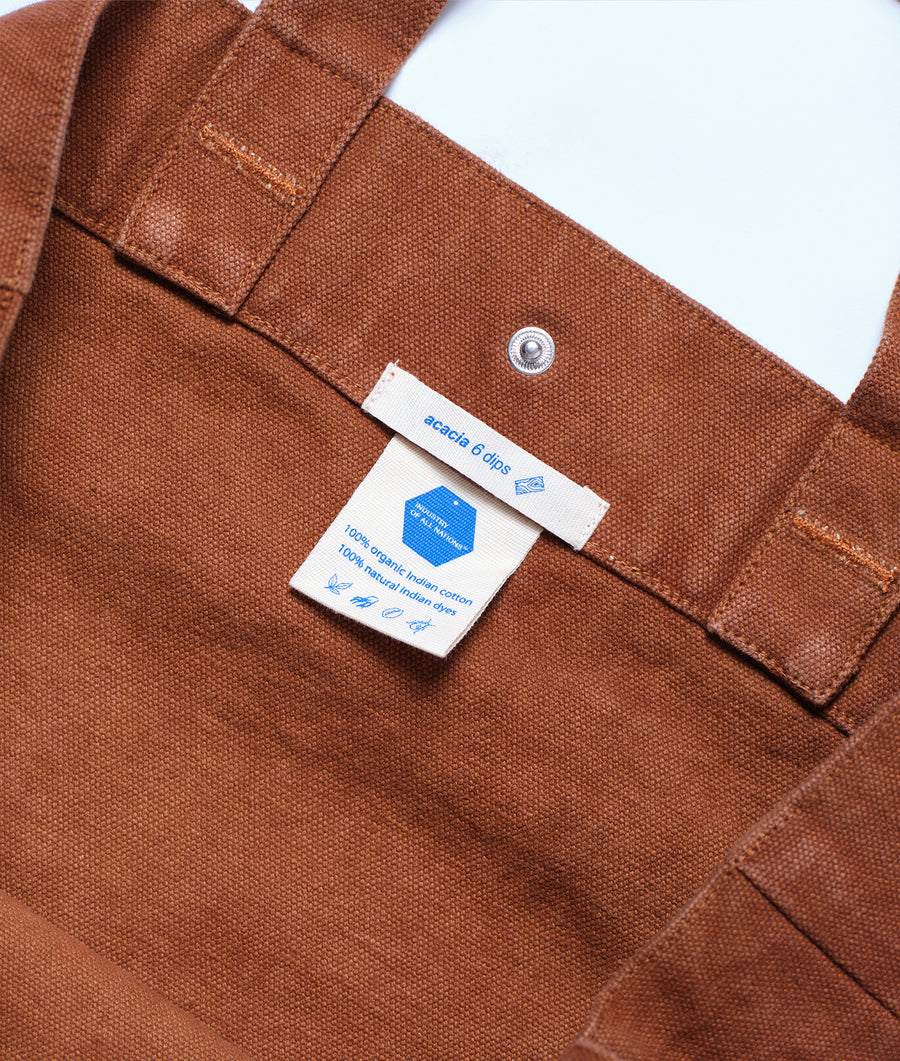A close-up detail shot of a brown organic cotton button-up shirt with a tag indicating it's from the Industry of All Nations brand.