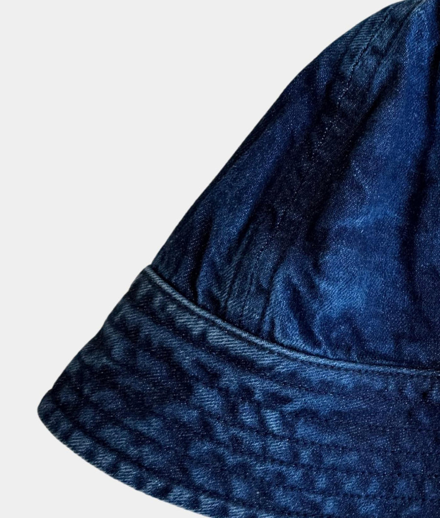 Close-up of a dark blue denim bucket hat showing the fabric texture and stitched brim against a light gray background.