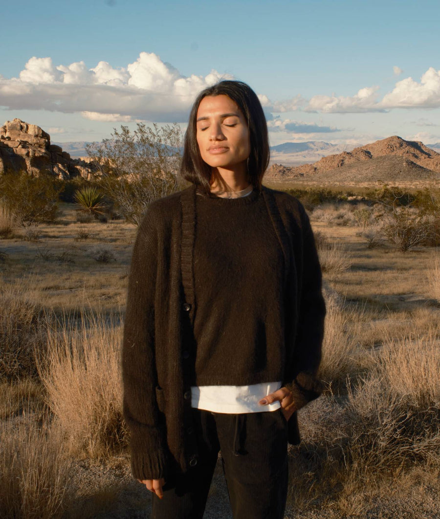 Woman wearing a dark olive green wool coat in a desert landscape - Industry of All Nations
