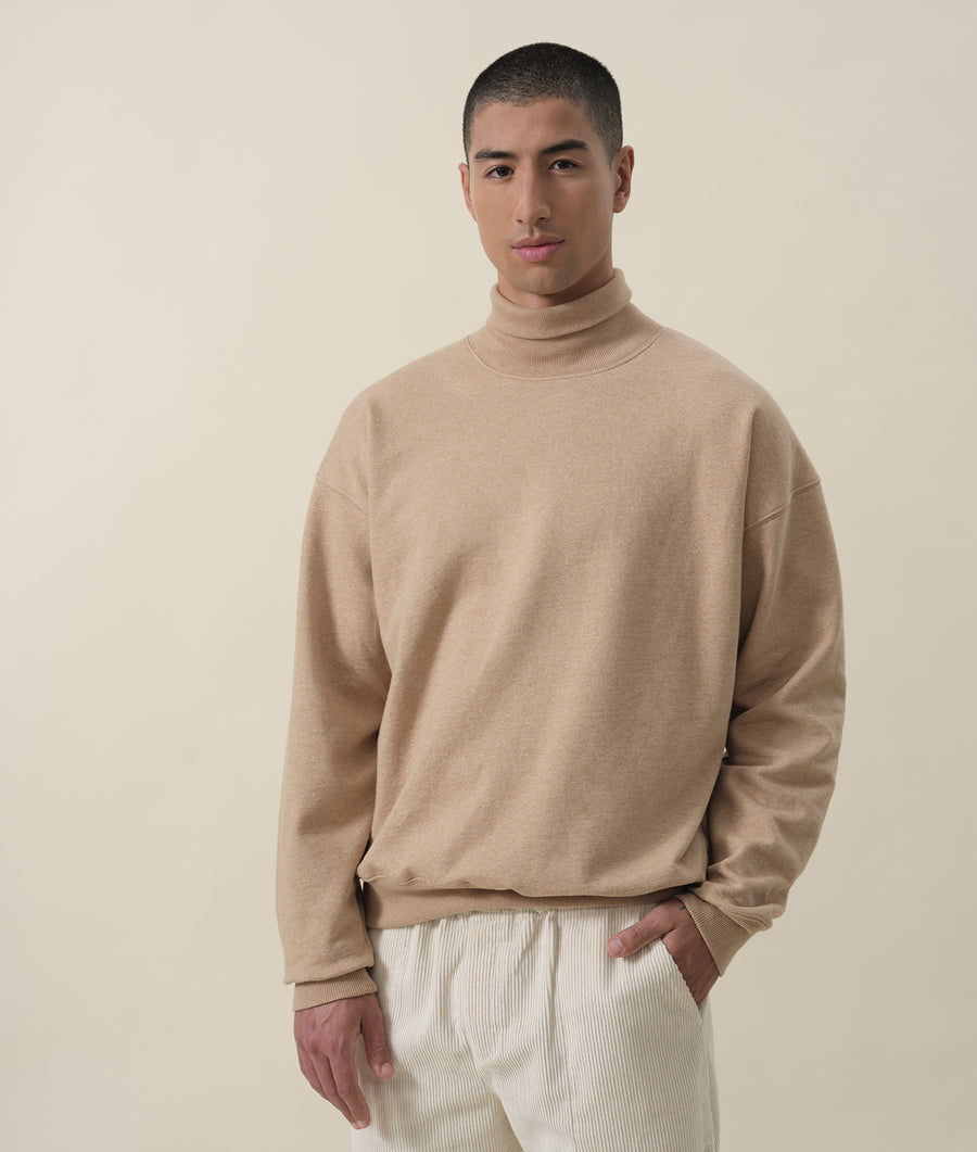 Man wearing a beige turtleneck sweater in a neutral studio setting - Industry of All Nations