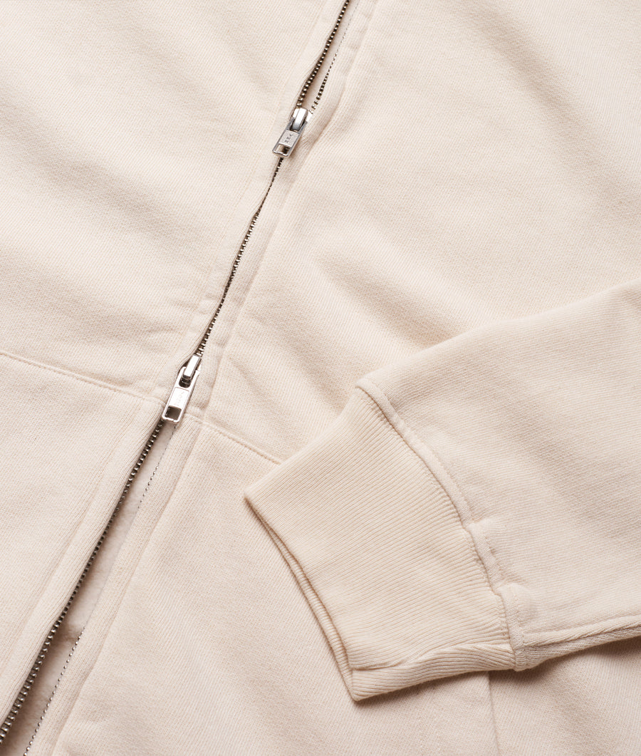 A close-up detail shot of a beige cotton sweatshirt with a zipper and ribbed cuffs - Industry of All Nations
