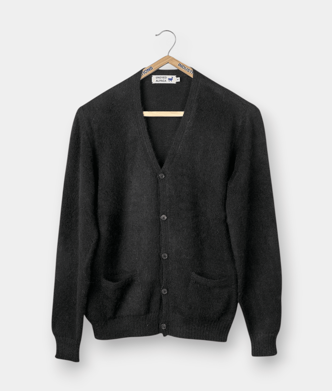 A black knit cardigan sweater displayed on a wooden hanger - Industry of All Nations.