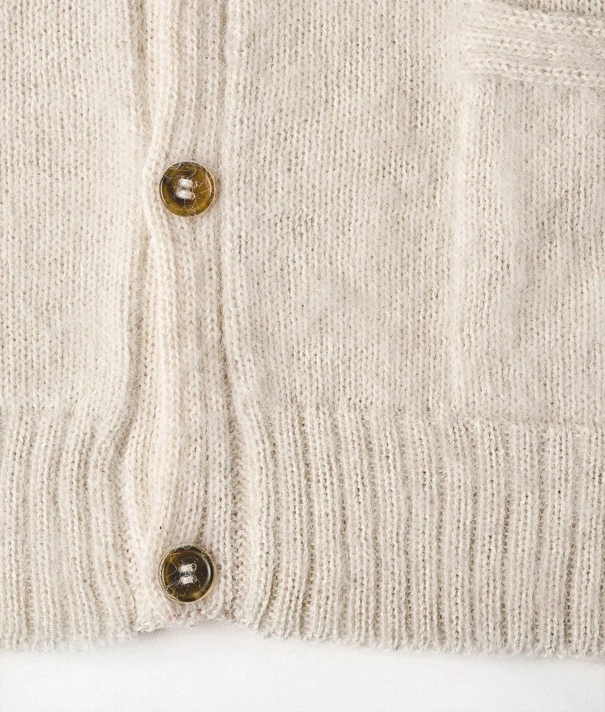 Close-up of a cream-colored knit cardigan sweater showing the ribbed texture, button closure, and a buttoned pocket.