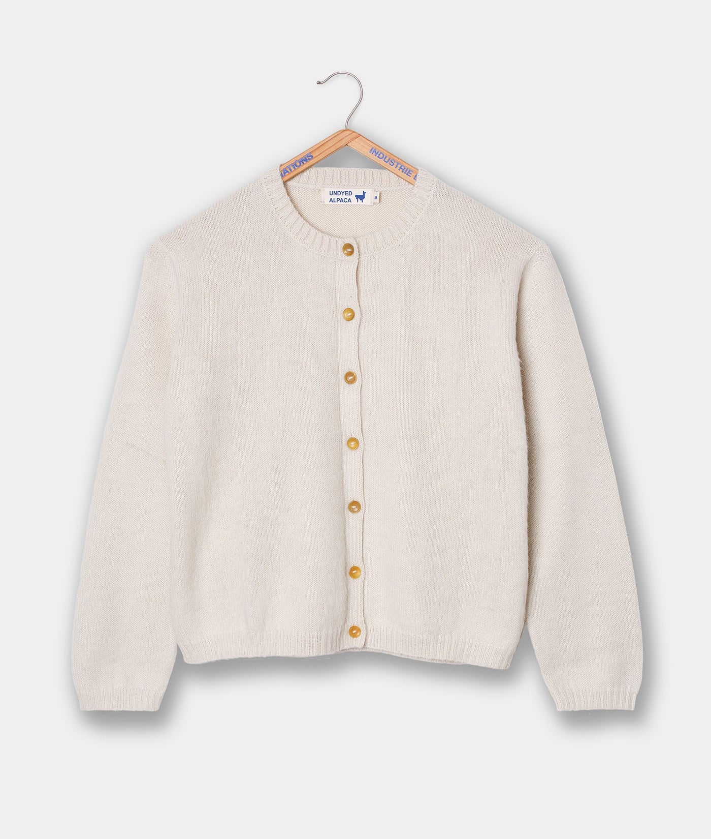 Cream-colored alpaca wool cardigan with wooden buttons displayed on a hanger - Industry of All Nations