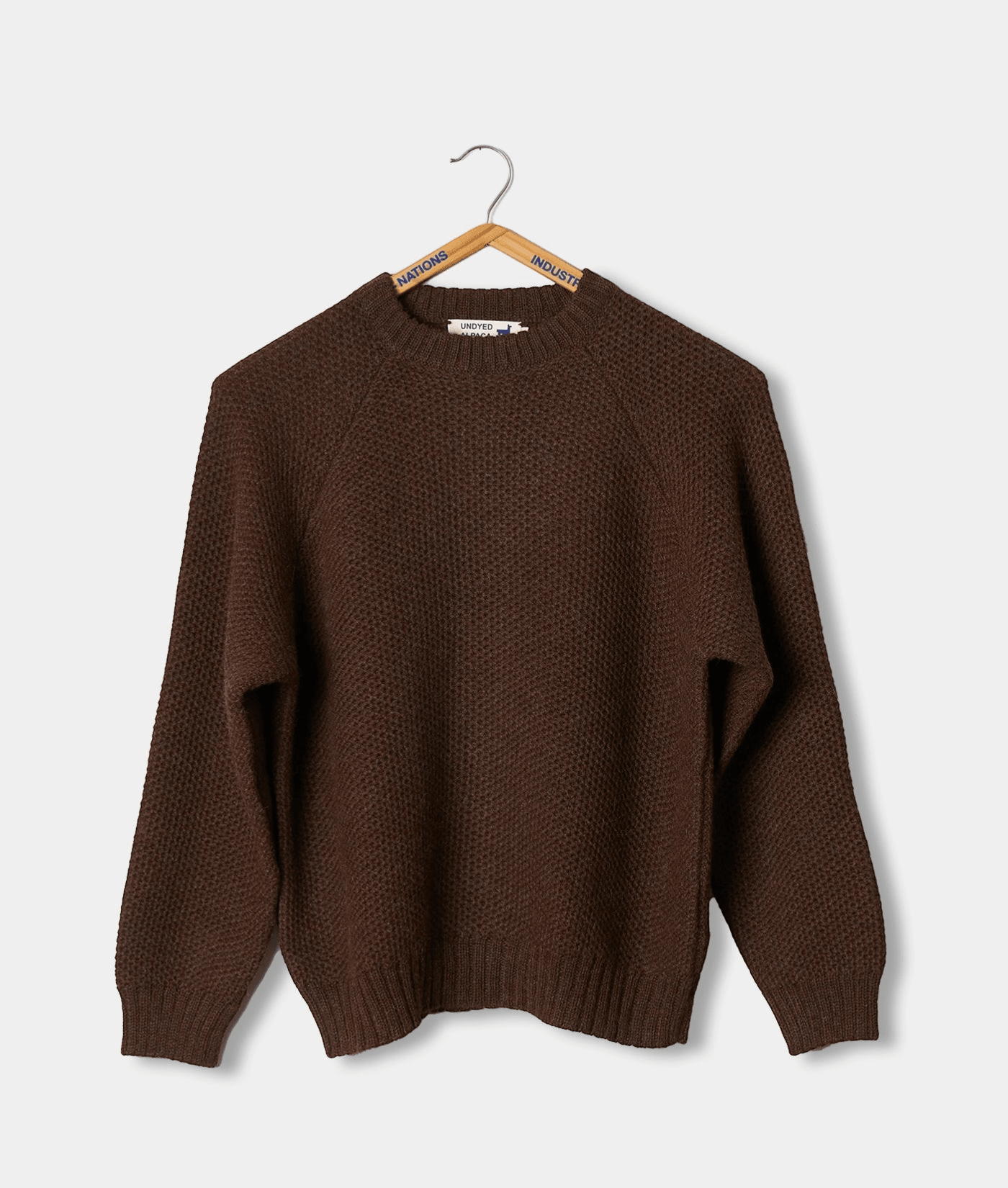 A brown knit sweater hanging on a wooden hanger with brand tags - Industry of All Nations