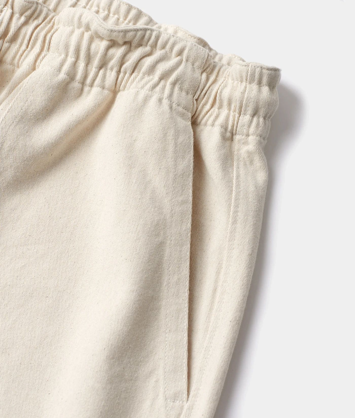 Close-up of a pair of off-white or cream-colored cotton pants, showing the elastic waistband and fabric texture against a light gray background.