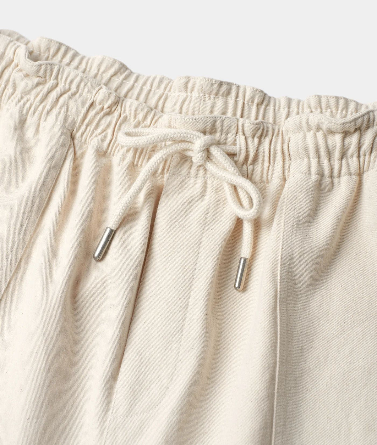 Close-up of cream-colored drawstring pants showing the elastic waistband and drawstring with silver metal tips.