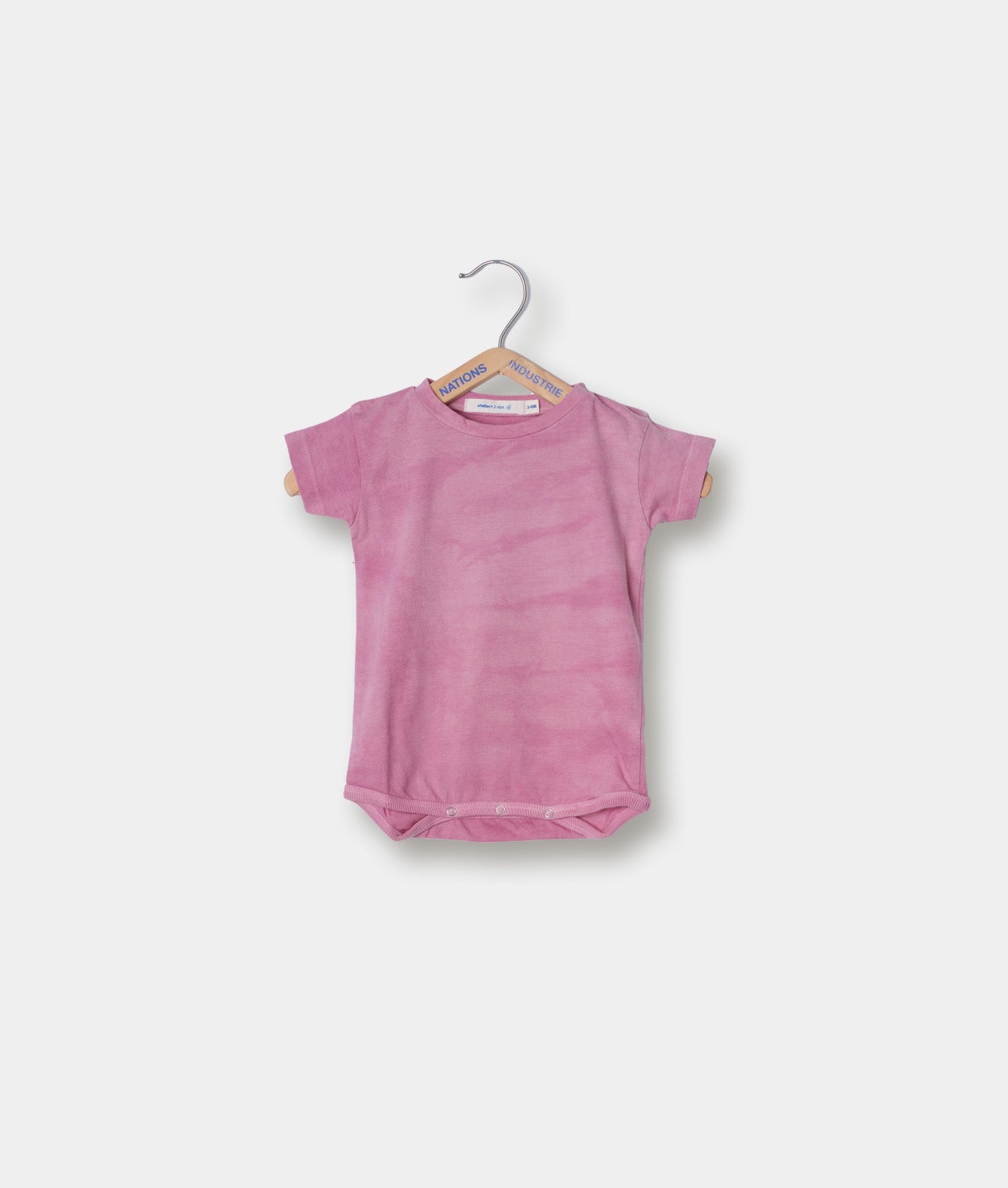 A plain pink/magenta onesie or bodysuit hanging on a grey wooden hanger - Industry of All Nations