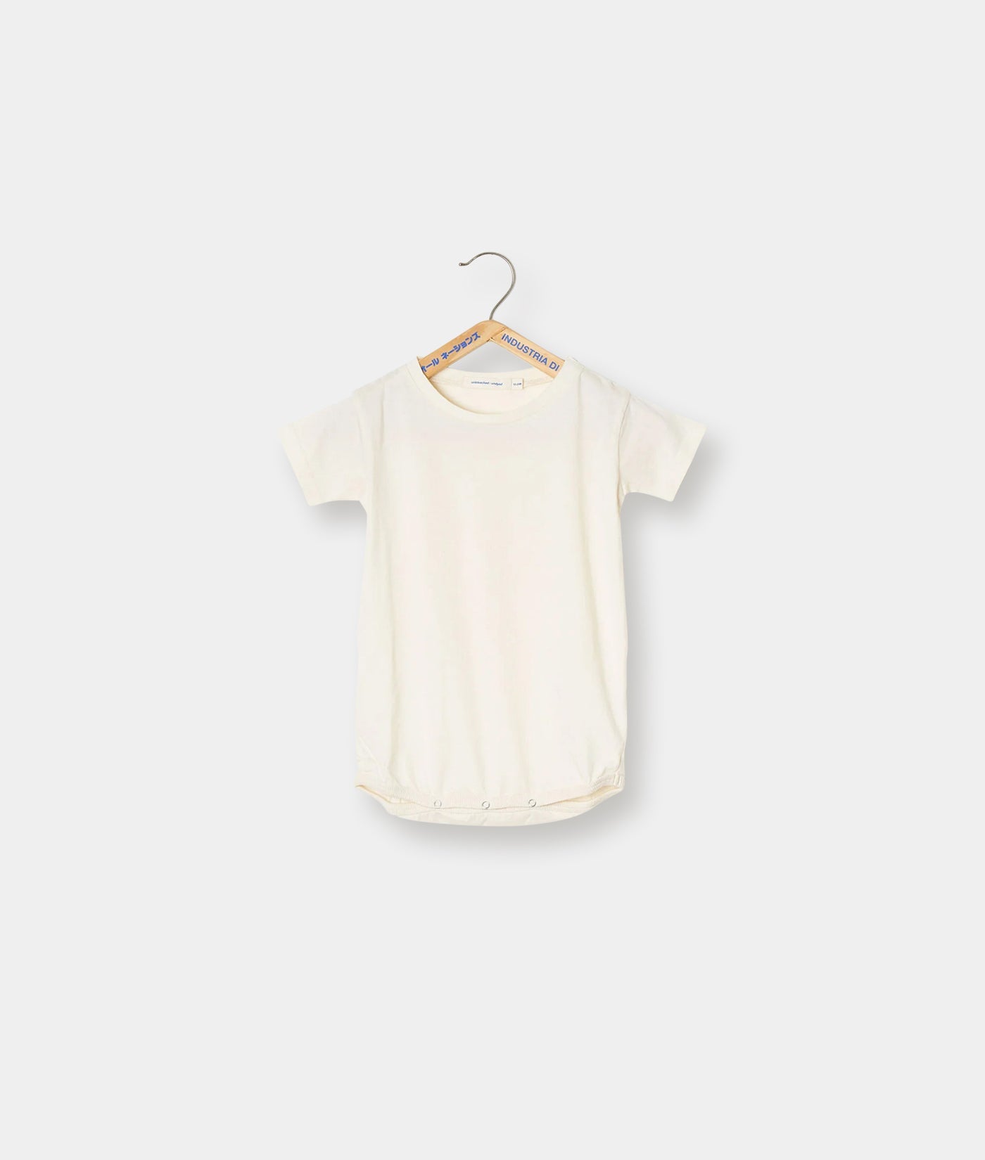 A plain, cream-colored onesie or bodysuit hanging on a hanger - Industry of All Nations