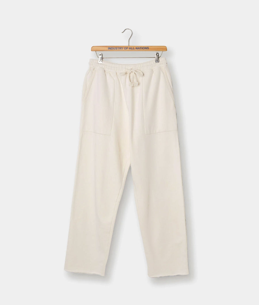 Cream-colored drawstring pants hanging on a wooden hanger with "Industry of All Nations" printed on the label - Industry of All Nations