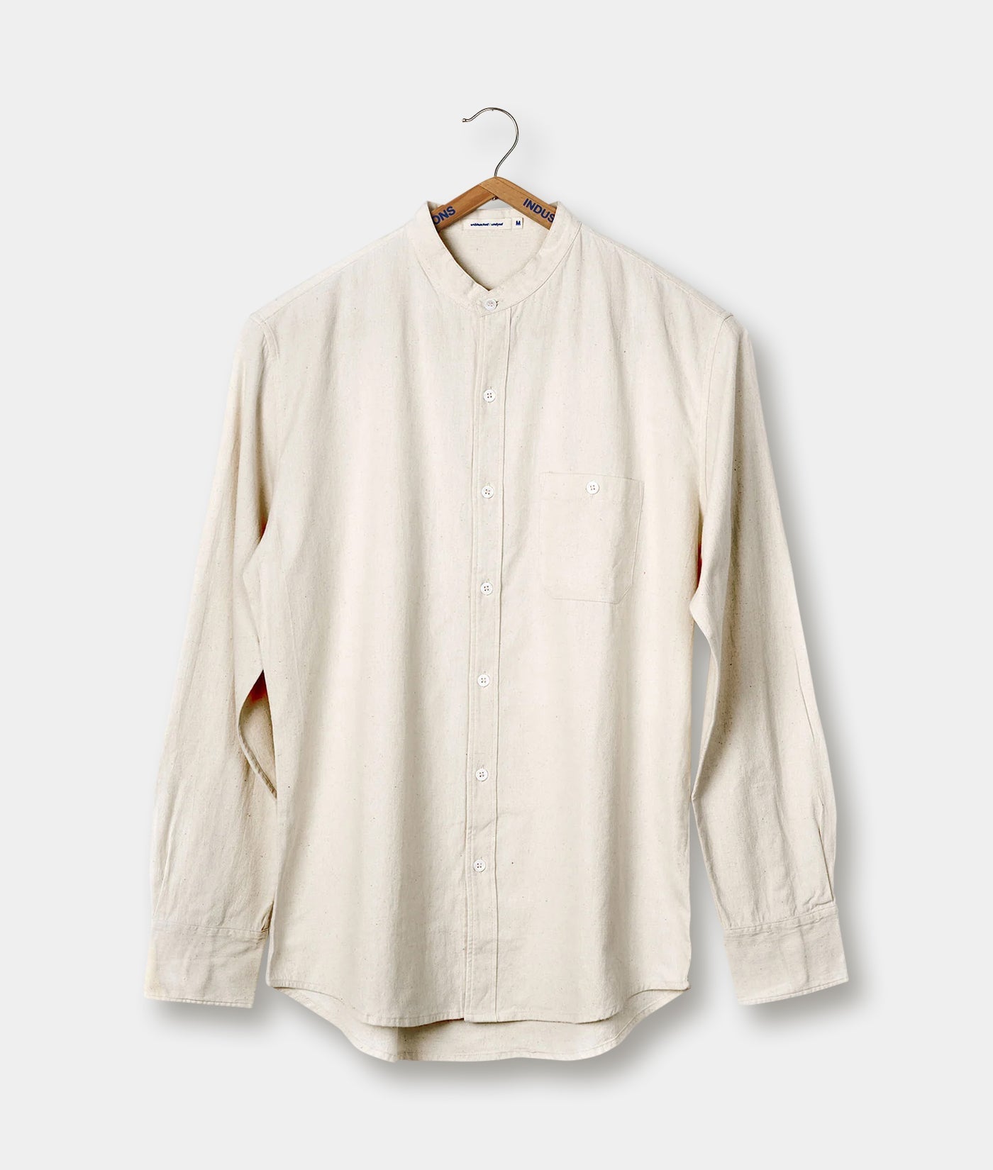 Cream-colored button-down shirt hanging on a wooden hanger - Industry of All Nations