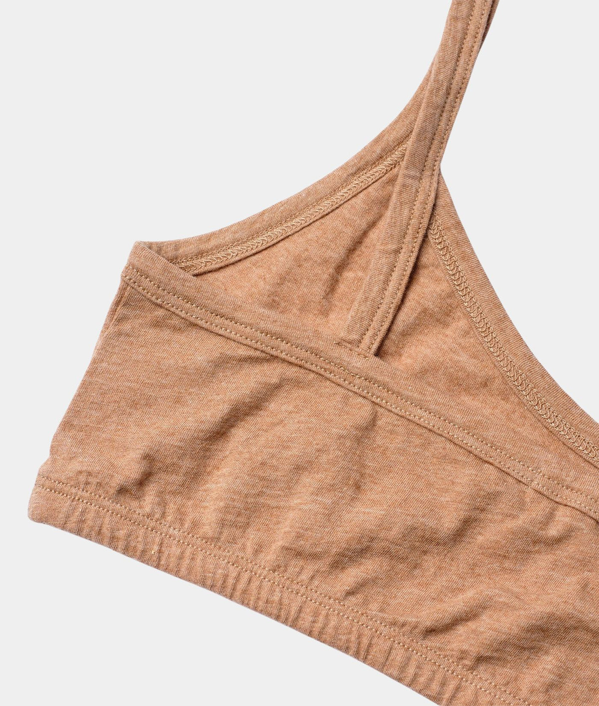 Close-up of a heathered tan sports bra strap and cup corner, showing the fabric texture and stitching against a light gray background.