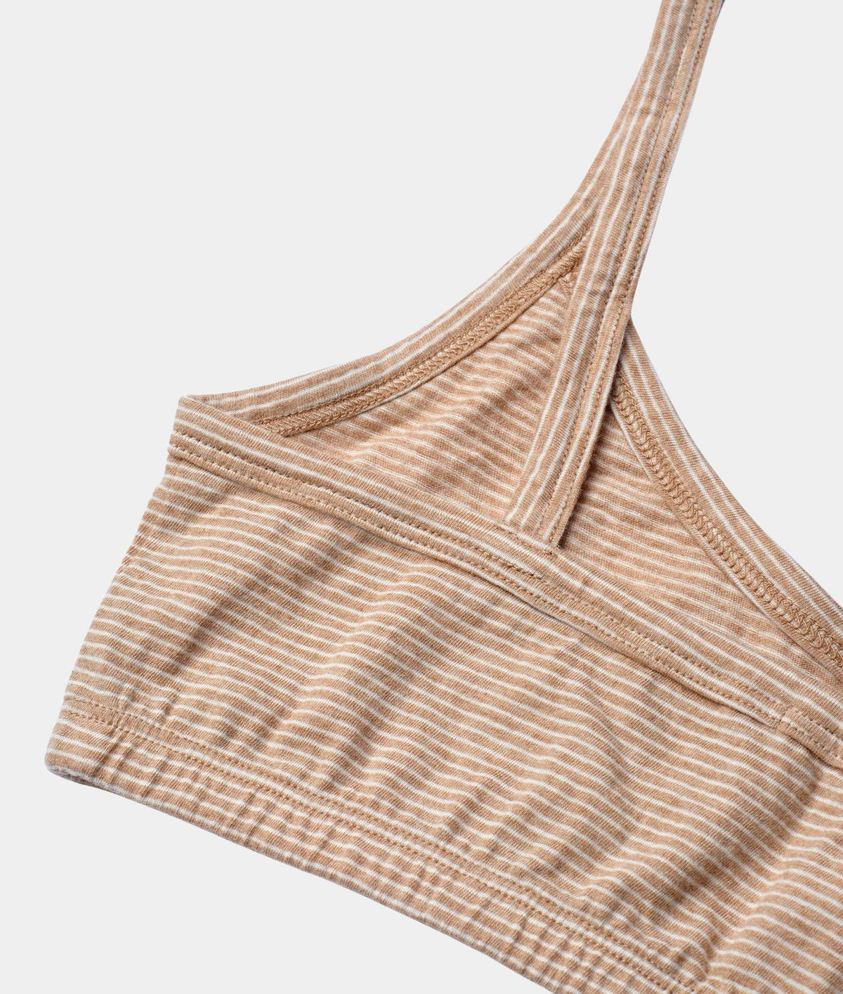 Close-up of a ribbed knit bralette in a warm beige and white stripe pattern, showing the underband and crossover shoulder straps against a light gray background.