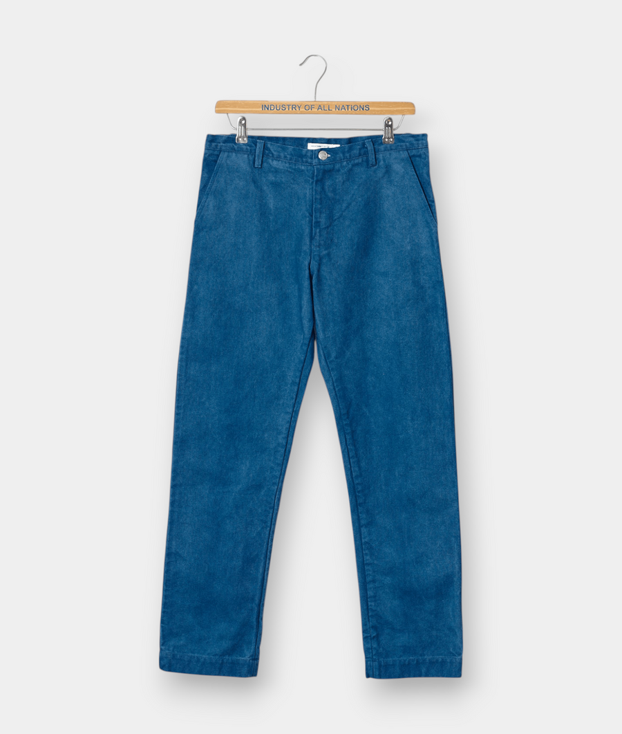 A pair of blue denim pants hanging on a wooden hanger with the text "Industry of All Nations" - Industry of All Nations