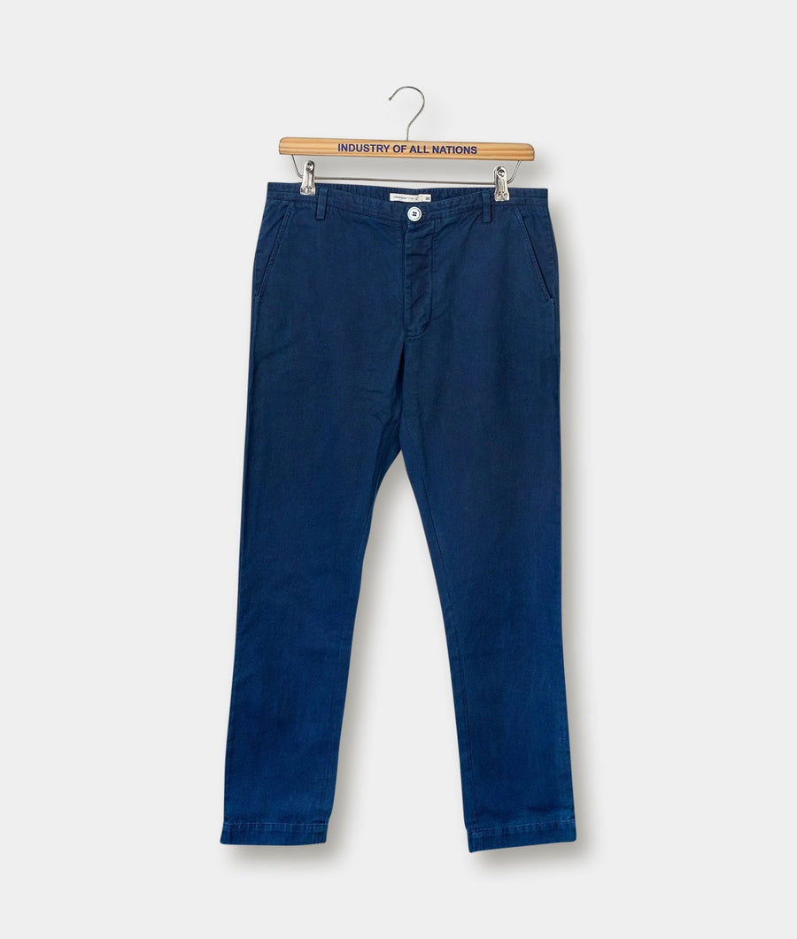 Navy blue cotton chinos hanging on a wooden hanger with "Industry of All Nations" branding - Industry of All Nations