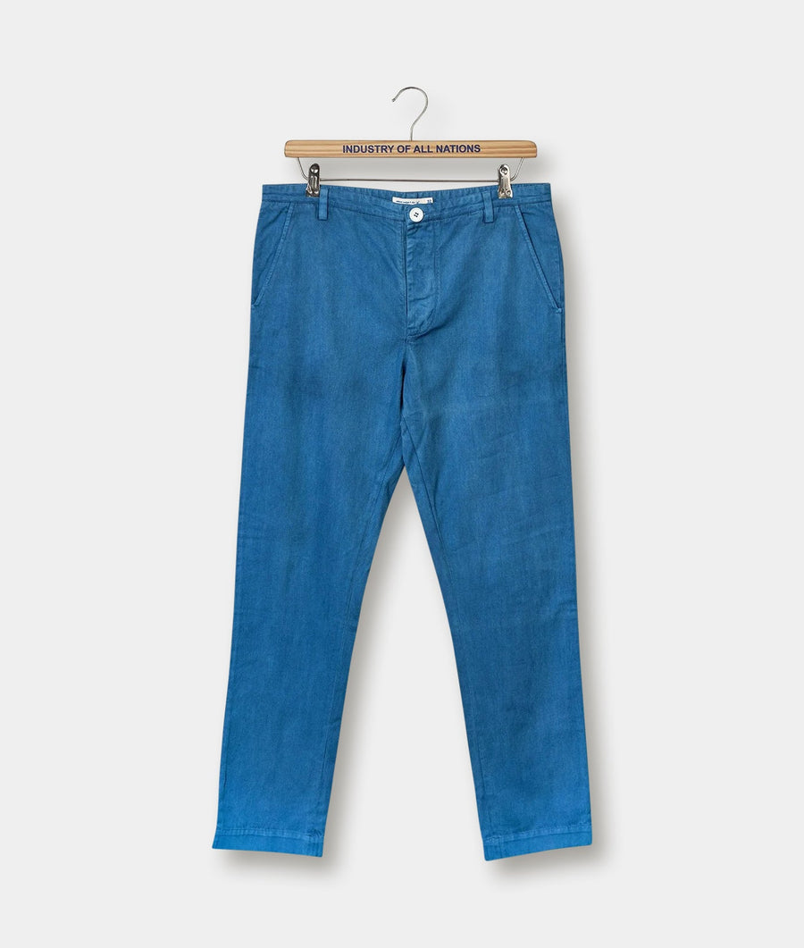 A pair of blue denim trousers hanging from a wooden hanger, with the text "Industry of All Nations" printed on it - Industry of All Nations