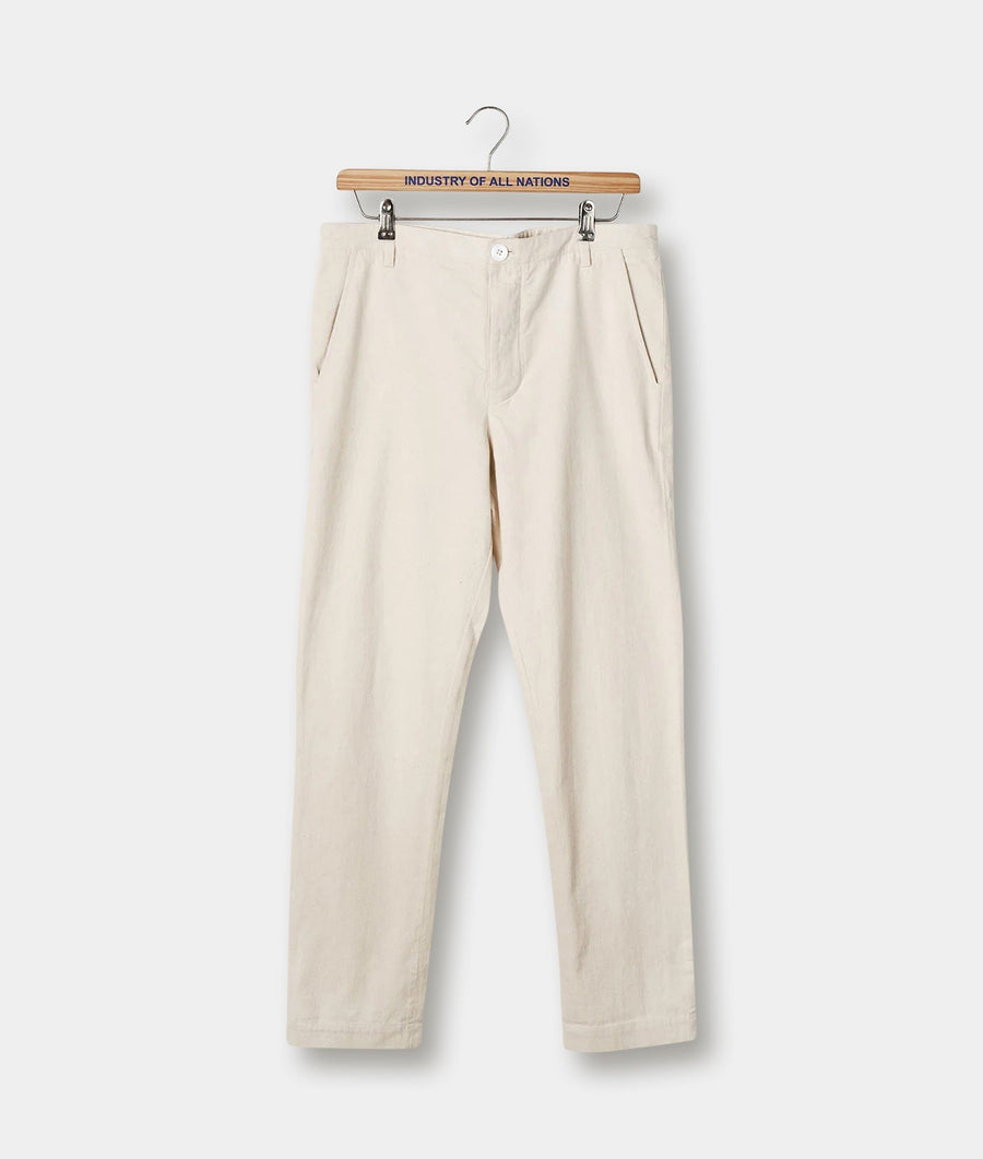Beige cotton pants displayed hanging from a wooden hanger with "Industry of All Nations" branded text - Industry of All Nations