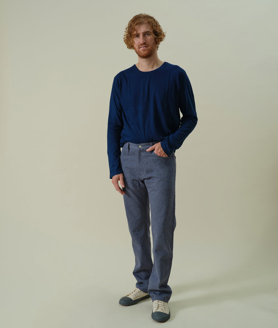 A man wearing a navy blue long-sleeved shirt and gray pants, standing with hands in pockets - Industry of All Nations