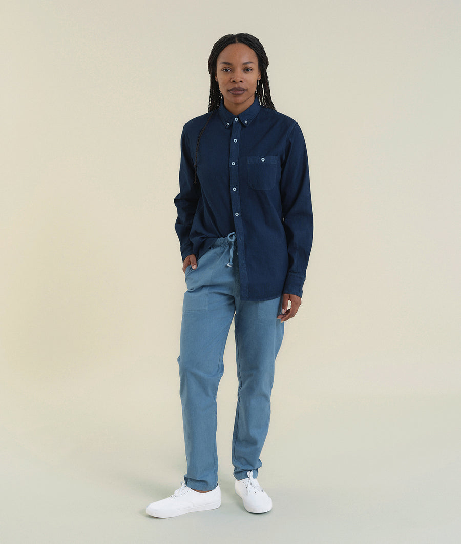 A person wearing a navy blue button-down shirt, gray drawstring pants, and white sneakers standing against a light background - Industry of All Nations