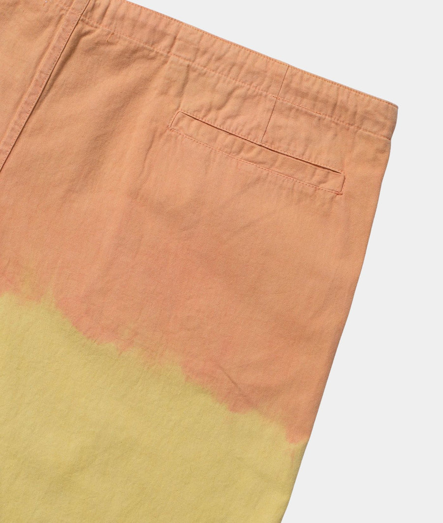 Close-up of a pair of shorts showing a diagonal color-blocked pattern with a peach top half and a yellow bottom half, featuring a welt pocket on the upper right side.