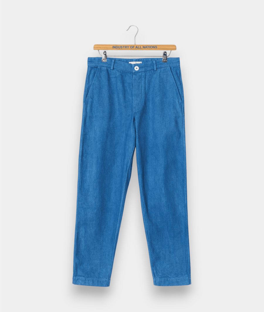 A pair of light blue denim pants hung on a wooden hanger with "Industry of All Nations" text displayed - Industry of All Nations