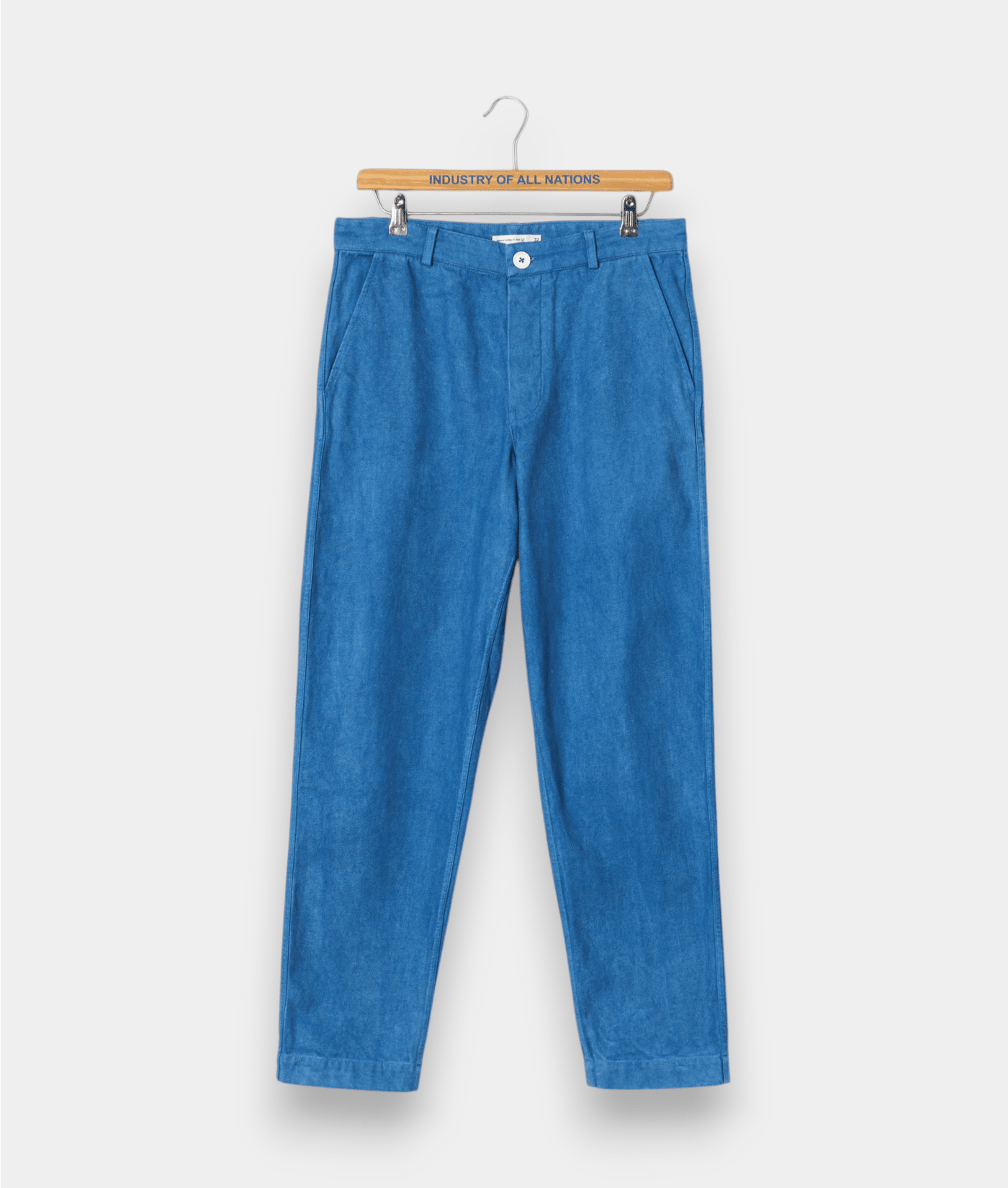 A pair of light blue denim pants hung on a wooden hanger with "Industry of All Nations" text displayed - Industry of All Nations